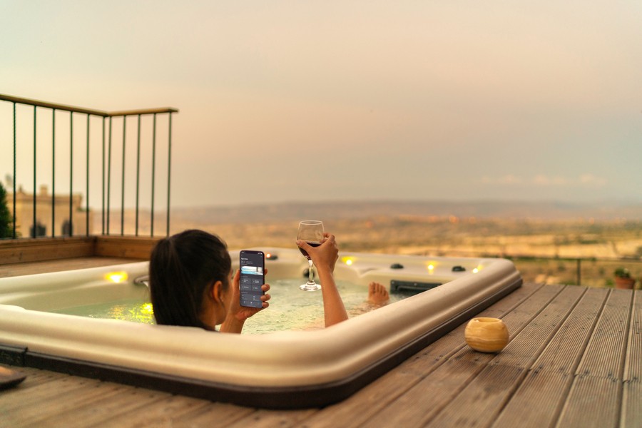 Woman in a jacuzzi in Arizona holding a glass of wine and phone with a smart home automation app. 