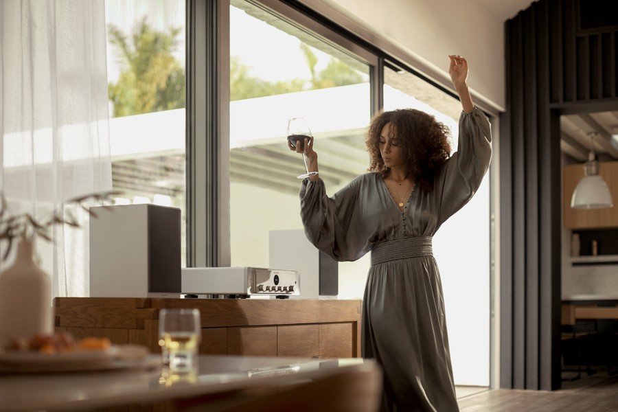 Woman holding a glass of wine and dancing beside her multi-room audio speakers. 